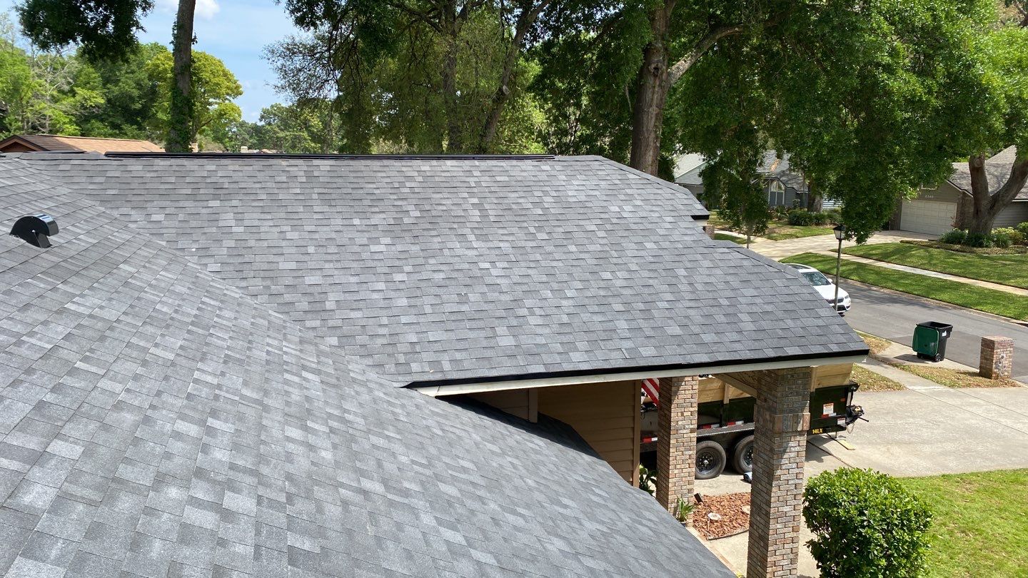 A gray shingled residential roof in a neighborhood.